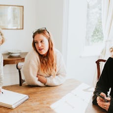 An adult woman sits at a dining table with her mom, who takes notes on a notepad.