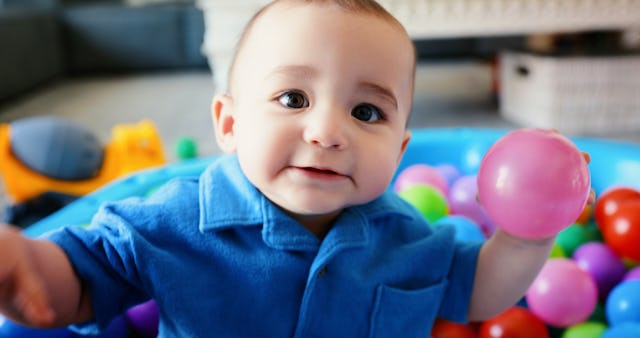 A baby sits in a kiddie pool filled with balls.