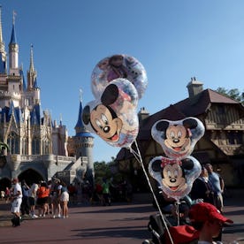 Cinderella Castle at Magic Kingdom with visitors walking and Mickey Mouse balloons attached to a str...