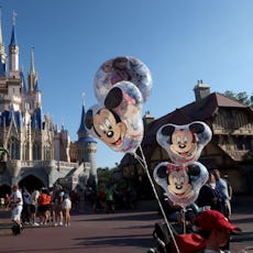 Cinderella Castle at Magic Kingdom with visitors walking and Mickey Mouse balloons attached to a str...