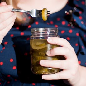 Person holding a jar of pickles and using a fork to lift one out, dressed in a polka dot top.