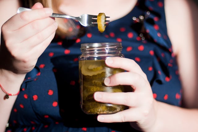 Person holding a jar of pickles and using a fork to lift one out, dressed in a polka dot top.