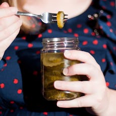 Person holding a jar of pickles and using a fork to lift one out, dressed in a polka dot top.