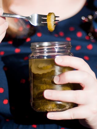 Person holding a jar of pickles and using a fork to lift one out, dressed in a polka dot top.