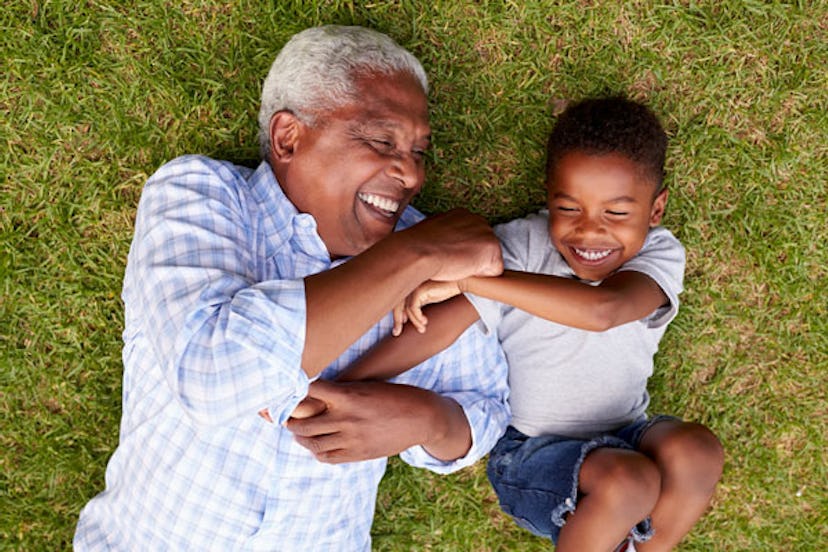 A grandpa laying on the grass with his grandson while smiling and playing