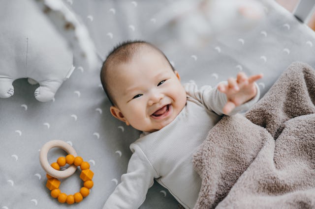 Portrait of a lovely Asian baby girl smiling sweetly while lying on the crib. She is raising her han...