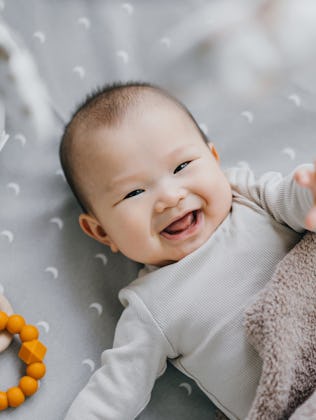 Portrait of a lovely Asian baby girl smiling sweetly while lying on the crib. She is raising her han...