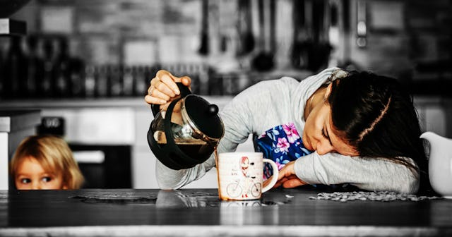 A single mom falling asleep while her child watches her pouring the coffee next to the cup. 