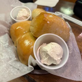 Three buttery Texas Roadhouse Rolls served on a paper liner with two small cups of whipped cinnamon ...