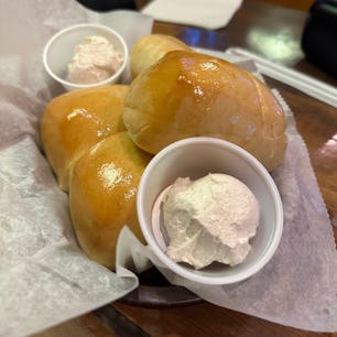 Three buttery Texas Roadhouse Rolls served on a paper liner with two small cups of whipped cinnamon ...