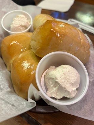 Three buttery Texas Roadhouse Rolls served on a paper liner with two small cups of whipped cinnamon ...