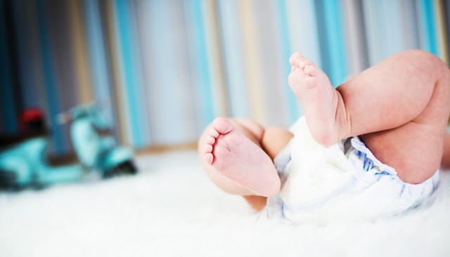 A baby in a diaper lying on a white carpet with a blue/brown/beige striped wall 