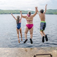 Woman, boy and girl plunging in water lake from the deck during summer day vacations