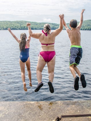 Woman, boy and girl plunging in water lake from the deck during summer day vacations